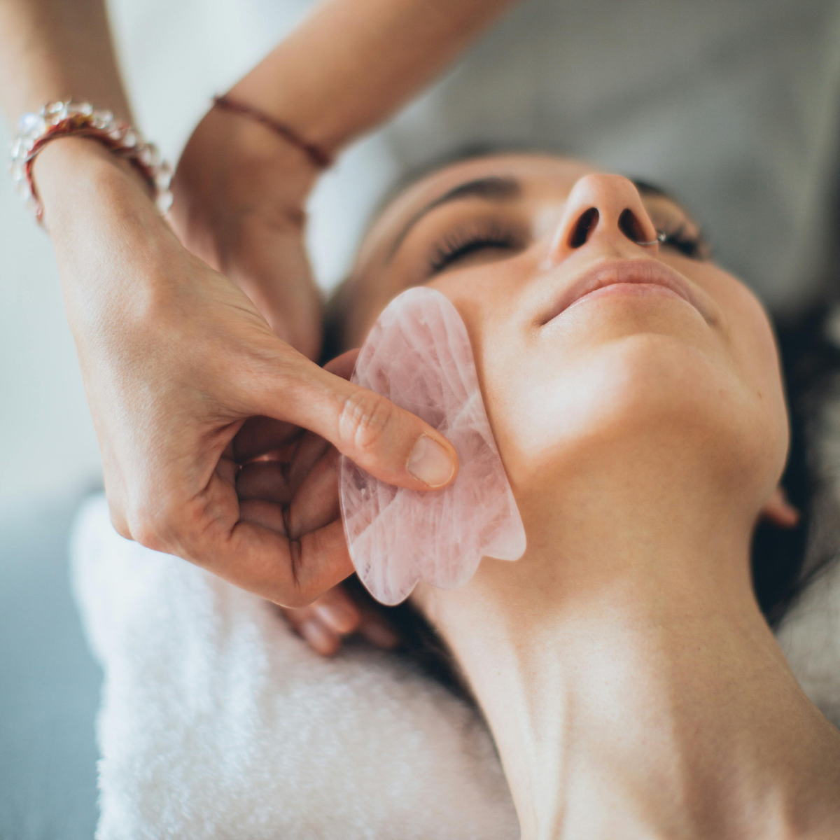 Gua sha kvarc ružičnjak na licu žene koja leži na tretmanu